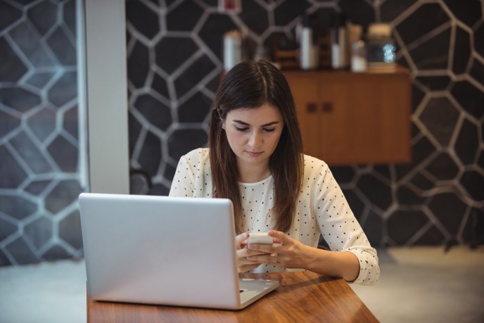 Businesswoman using mobile phone with laptop on table in café